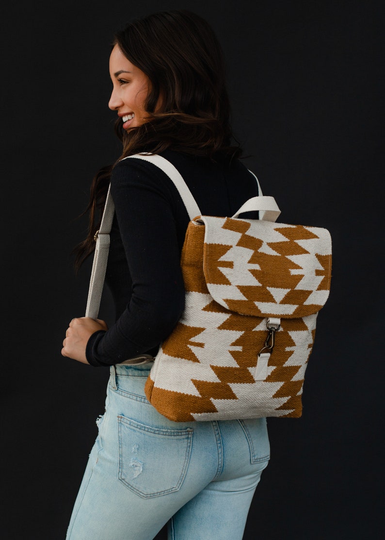 May include: A brown and white geometric patterned backpack with a white strap. The backpack has a flap with a buckle closure.