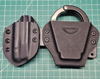 May include: A black leather holster with a metal handcuff holder. The holster has multiple screws and is designed to be worn on a belt.