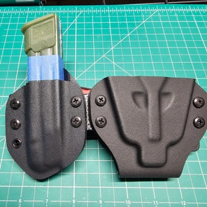 May include: Two black leather holsters with a magazine holder on the left. The holsters have multiple screws and are designed to be attached to a belt.