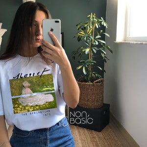 May include: White t-shirt with a graphic print of a painting by Monet. The painting is titled "The Springtime 1872".