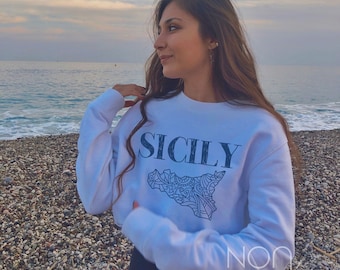 May include: A white sweatshirt with a blue graphic of the island of Sicily and the word "SICILY" printed in blue. The sweatshirt also has the words "NON BASIC" printed in blue on the bottom.