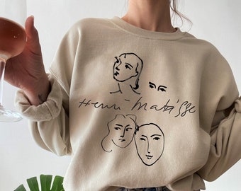 May include: A beige sweatshirt with a black graphic print of three abstract faces and the text "#henri-matisse".