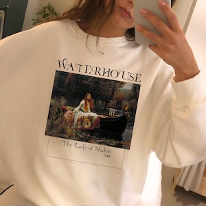 May include: White sweatshirt with a graphic print of a painting by John William Waterhouse titled "The Lady of Shalott" from 1888. The text "WATERHOUSE" is printed above the painting.