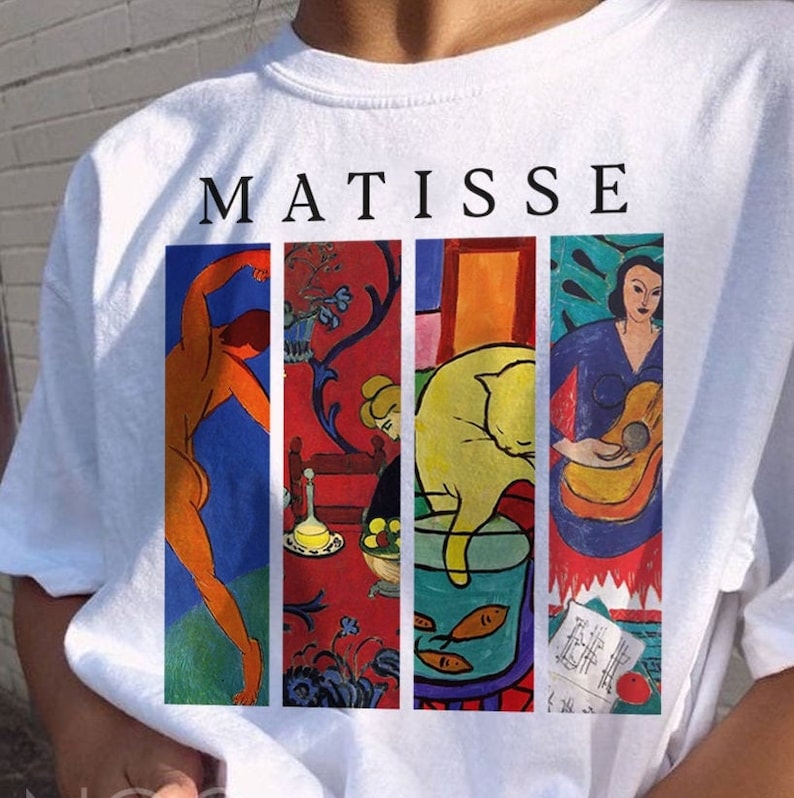 May include: White t-shirt with a colorful print of four Matisse paintings. The paintings include a nude man, a woman playing a guitar, a cat in a bowl of water, and a woman sitting in a room. The text "MATISSE" is printed above the paintings.
