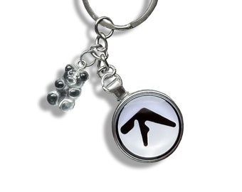 May include: A silver keychain with a black and white logo charm and a small gummy bear charm. The logo is a stylized arrow pointing upwards.