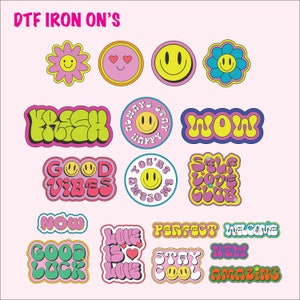 May include: A collection of colorful DTF iron-on transfers with various designs. The transfers include smiley faces, flowers, and phrases like "Good Vibes," "Love is Love," and "Amazing." The text "DTF IRON ON'S" is at the top.