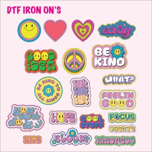 May include: A collection of colorful DTF iron-on transfers with various designs and text. Designs include smiley faces, hearts, peace signs, and phrases like "Easy," "Be Kind," and "Good Vibes." The text "DTF IRON ON'S" is at the top.
