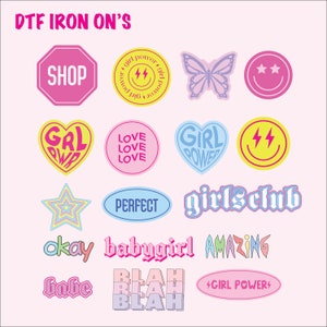 May include: A collection of DTF iron-on transfers with various designs and text. Includes a pink stop sign with "SHOP", a yellow circle with a lightning bolt, a butterfly, a smiley face, hearts, stars, and the words "GIRLS CLUB", "BABYGIRL", and "AMAZING".