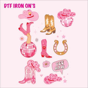May include: A collection of pink and tan cowboy-themed iron-on designs. The designs include cowboy boots, hats, a horseshoe, a disco ball, and the text "Yee Haw". The text "DTF IRON ON'S" is at the top.