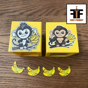May include: Two yellow square boxes featuring cartoon monkey illustrations, one with a smiling monkey holding bananas and the other with a muscular, angry monkey holding bananas. Four small yellow banana-shaped tokens with the text +1 Life are included.