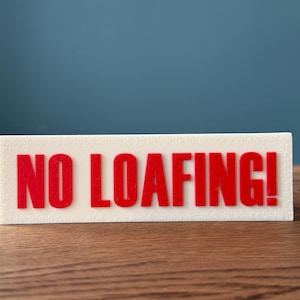 May include: White sign with red lettering that says "NO LOAFING!"