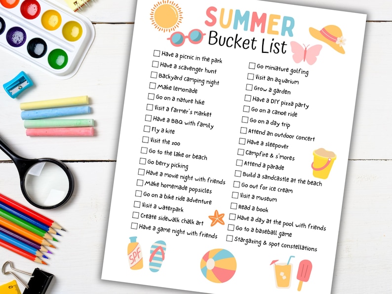 May include: A printed "Summer Bucket List" with colorful illustrations of a sun, sunglasses, and other summer-themed icons. The list includes activities like picnics, swimming, and stargazing. Watercolor paints and pencils are in the background.