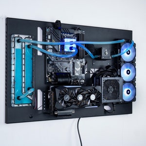 Puede incluir: Una caja de ordenador negra con un sistema de refrigeración por agua personalizado. La caja tiene un panel de acrílico transparente en el lateral, que revela los componentes del interior. El sistema de refrigeración por agua incluye un depósito, una bomba y un radiador. Los componentes están iluminados con LEDs azules.
