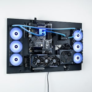 May include: A black computer case with a clear window revealing the motherboard, graphics cards, and fans. The fans are illuminated with blue LEDs. The case is mounted on a wall.