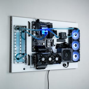 May include: A white wall-mounted computer system with a custom water-cooling loop. The system features a motherboard, graphics card, and multiple fans with blue LED lighting.