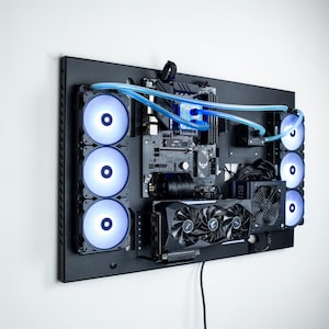 May include: A black computer case with a motherboard, graphics card, and multiple fans. The case is mounted on a wall and has blue tubing running through it.
