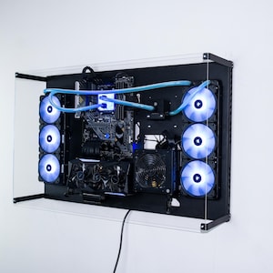 May include: A black computer case with a clear acrylic front panel. The case is mounted on a wall and has multiple blue LED fans visible. The case is open and shows the internal components of the computer, including the motherboard, graphics card, and power supply.
