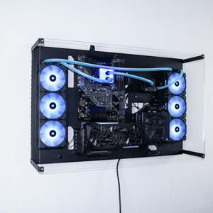 May include: A black computer case with a clear acrylic front panel. The case is mounted on a wall and has multiple blue LED fans visible. The case is open and shows the internal components of the computer, including the motherboard, graphics card, and cooling system.