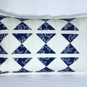 Könnte beinhalten: Rechteckiges Kissen mit einem Steppmuster. Das Kissen hat einen weißen Hintergrund mit abwechselnden Reihen aus weißen und marineblauen Rauten. Die marineblauen Rauten haben ein Blumenmuster. Zwei dunkle Knöpfe befinden sich an der Seite.