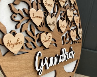 May include: A wooden heart-shaped family tree with the word "Grandkids" written in white letters. The tree is decorated with small wooden hearts, each with a name written on it, including "Haydeir", "Jude", "Braddon", "Jaxon", "Leurvor", "Isabelle", "Genesis", "Jesse", "Gracen", "Josiah", "Luca", "Joplin", "Joria", and "Amelia".