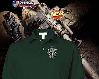 Può includere: Una polo verde scuro con un emblema ricamato in bianco sul petto sinistro. L'emblema raffigura due frecce incrociate, un pugnale e un globo con il testo DE OPPRESSO LIBER. La maglia presenta un colletto, due bottoni e maniche corte.