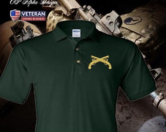 Può includere: Polo verde scuro con un emblema dorato di pistole incrociate. La camicia ha un colletto button-down e maniche corte. L'immagine include anche il testo "OP Alpha Designs" e un logo "Veteran Owned Business".
