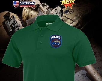 Può includere: Polo verde con abbottonatura a tre bottoni e colletto. La maglietta presenta una toppa ricamata con la scritta "POLICE NYPD EMERGENCY SQUAD". La maglietta ha anche la scritta "BAW" sul colletto.