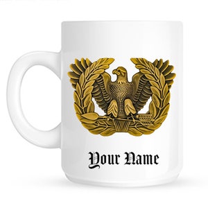 May include: White ceramic mug with a gold eagle and laurel wreath design. The text "Your Name" is printed below the design.