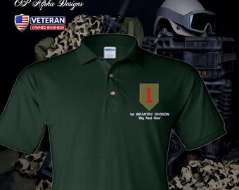Può includere: Polo verde scuro con una toppa ricamata con un numero 1 rosso su sfondo beige. Il testo "1st INFANTRY DIVISION 'Big Red One'" è sotto. La maglia ha una chiusura a tre bottoni.