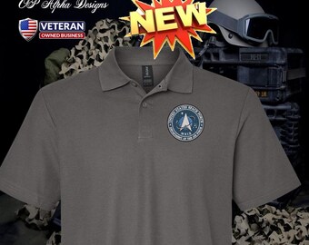 Può includere: Polo grigio con l'emblema della United States Space Force sul petto sinistro. La maglietta ha una chiusura a tre bottoni e maniche corte. Una grafica "NEW" è sopra la maglietta. Da OP Alpha Designs, un'azienda di proprietà di veterani.