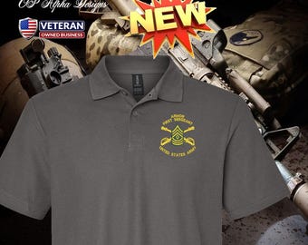 Può includere: Polo grigio con la scritta dorata "Armor First Sergeant United States Army". La maglietta ha un colletto button-down e un piccolo stemma sul petto. L'immagine include anche una grafica "NUOVO" e un logo "Veteran Owned Business".