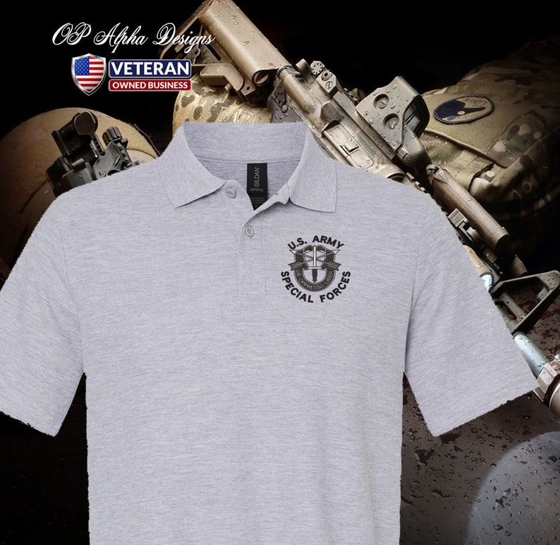 Pu&ograve; includere: Una polo grigia con una toppa ricamata nera che dice "U.S. ARMY SPECIAL FORCES" e presenta un'immagine stilizzata di un soldato con un fucile e un paracadute. La polo &egrave; su uno sfondo mimetico.