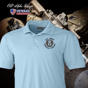 Pu&ograve; includere: Una polo blu chiaro con una toppa ricamata nera che dice "U.S. ARMY SPECIAL FORCES" e presenta un pugnale stilizzato e ali.