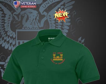 Può includere: Una polo verde scuro con ricamo dorato con la scritta "U.S. ARMY CORPS OF ENGINEERS". La camicia presenta anche la grafica "NEW" e il logo "VETERAN OWNED BUSINESS".