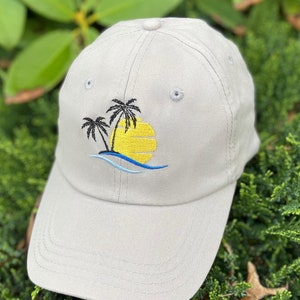 May include: A gray baseball cap with an embroidered design of palm trees and a yellow sun setting over a blue wave.