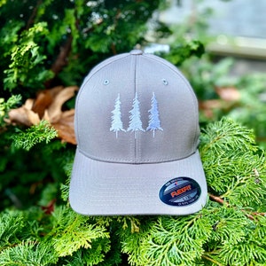 May include: A gray baseball cap with an embroidered design of three white pine trees. The cap has a Flexfit label on the back.