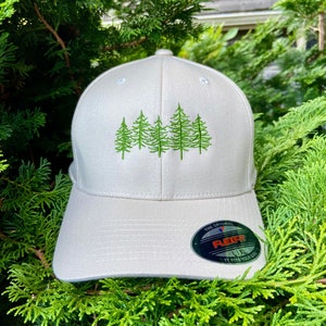 May include: A beige baseball cap with an embroidered design of five green pine trees. The cap has a black Flexfit label with the text "The Original Flexfit L/XL It Fits Your Life".