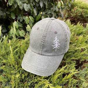 May include: A dark green baseball cap with a white embroidered pine tree design.