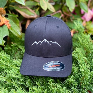 May include: Black baseball cap with a white mountain range embroidered on the front. The cap has a Flexfit label with the text "The Original Flexfit L/XL It Fits Your Life".