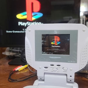 Könnte beinhalten: Eine weiße PlayStation Portable mit einem eingebauten Bildschirm, der das PlayStation-Logo und den Text "PlayStation. Licensed by Sony Computer Entertainment Inc." anzeigt.