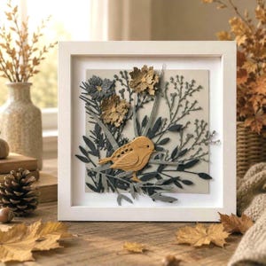 May include: A framed artwork featuring a tan bird perched on a branch, surrounded by gray and tan paper-cut flowers and foliage. The artwork is set against a neutral background within a white square frame, creating a nature-inspired decorative piece.