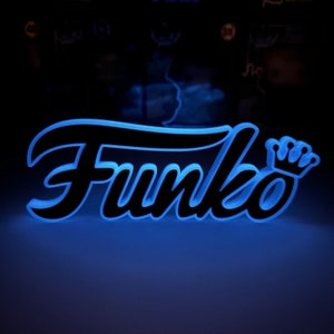May include: A glowing sign with the word "Funko" in a stylized font, featuring a crown icon. The sign has a black font with a bright blue outline, creating a neon effect against a dark background.