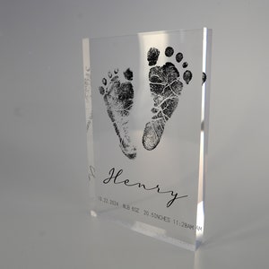 Op de afbeelding: Een heldere acrylblok met een zwarte inktindruk van babyvoetjes. De blok bevat ook de naam "Henry", de datum "10.22.2024", het gewicht "8.8 LB 6OZ", de lengte "20.5 INCHES" en de tijd "11:28AM".