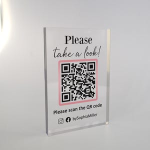 Könnte beinhalten: Ein weißes Acrylschild mit schwarzem Text, der "Bitte schauen Sie sich um!" lautet, und einem rosa-schwarzen QR-Code. Unter dem QR-Code befindet sich der Text "Bitte scannen Sie den QR-Code" und ein Social-Media-Symbol mit dem Text "bySophiaMiller".
