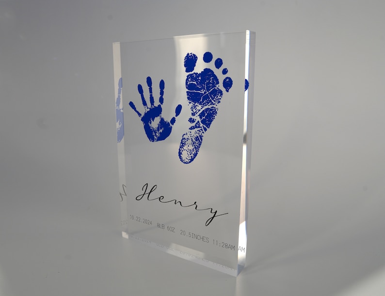 Op de afbeelding: Een heldere acrylblok met een blauwe handafdruk en voetafdruk, de naam "Henry" in cursief, en de datum "10.22.2024", het gewicht "8lb 5oz", de lengte "20.5 inch", en de tijd "11:28AM".