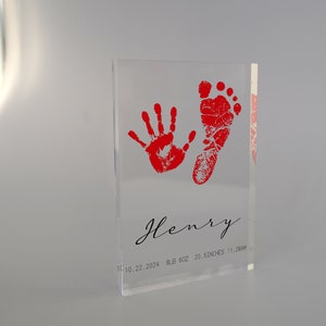 Op de afbeelding: Een heldere acrylblok met rode hand- en voetafdrukken. De blok heeft de naam "Henry" gegraveerd, samen met de datum "11.10.22.2024", het gewicht "8LB 6OZ", de lengte "20.5 INCHES" en de tijd "11:28AM".