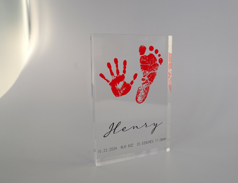 Op de afbeelding: Een heldere acrylblok met rode hand- en voetafdrukken. De blok heeft de naam "Henry" gegraveerd, samen met de datum "11.10.22.2024", het gewicht "8LB 6OZ", de lengte "20.5 INCHES" en de tijd "11:28AM".