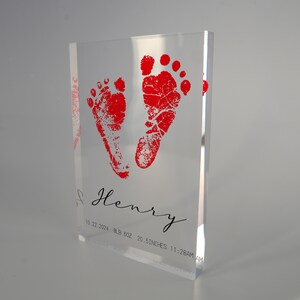 Op de afbeelding: Een heldere acrylblok met rode babyvoetjes en de naam "Henry" gegraveerd. De datum "10.22.2024", "BLB 6.02", "20.5 DUIM", en "11:28AM" zijn ook gegraveerd.