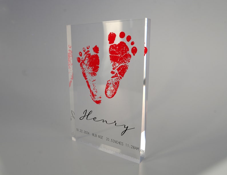 Op de afbeelding: Een heldere acrylblok met rode babyvoetjes en de naam "Henry" gegraveerd. De datum "10.22.2024", "BLB 6.02", "20.5 DUIM", en "11:28AM" zijn ook gegraveerd.