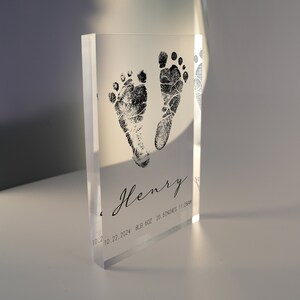 Op de afbeelding: Helder acrylblok met zwarte inkt baby-voetafdrukken en de naam "Henry" samen met de datum "10.22.2024", het gewicht "8,8 oz" en de lengte "20,5 inch".